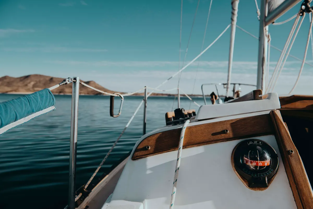 View across the deck of a sailing boat towards a bright coastline