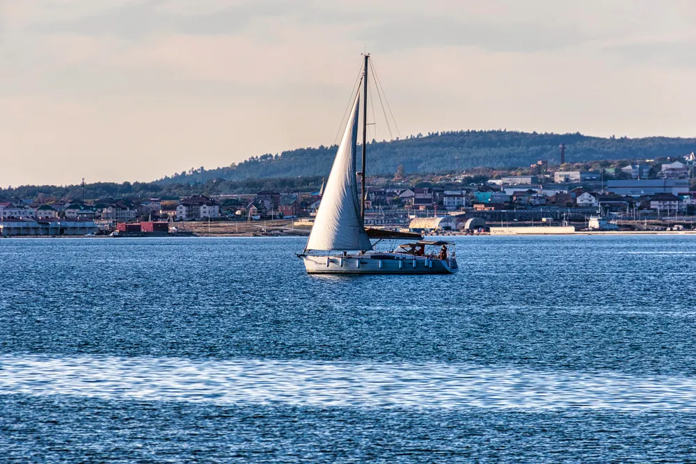 A sailing boat on calm blue water with a coastal town behind