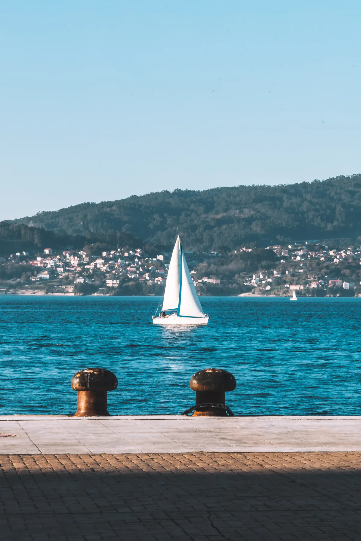 Sailing boat crossing a wide bay with a coastal town behind
